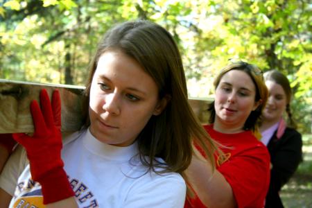 Elizabeth Blevins, sophomore political science major, Lauren Bogdan, junior Biblical studies major, and Sarah Conway, senior chemistry major, team together to transport a long cedar plank to a bog bridge construction area during Day of Remembrance.