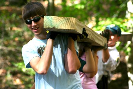 Chad Keathley, junior theology major, helps to carry a cedar plank for placement in the construction of a simple bog bridge at Pinson Mounds.
