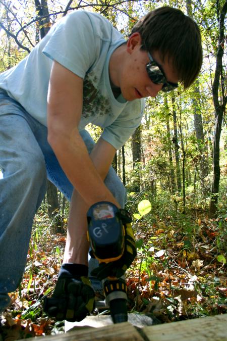 Chad Keathley, junior theology major, drills a hole in a bog bridge sleeper where a steel ground stake (rebar) will then be placed.