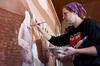 Angela McDaniel, art department secretary, adds detail to the mural on a wall at Daddy's Kitchen Table Soup Kitchen during Campus and Community Day. - Photo by Megan Bailey