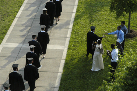 Graduates file onto the Great Lawn at the beginning of the graduation ceremony while one graduate jumps out to say hello to a friend.