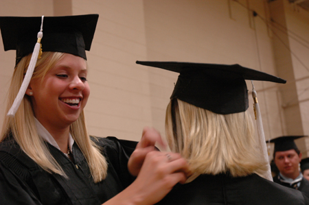 Public relations graduate Jill Martin assists fellow public relations graduate Amanda Jones prior to the spring graduation ceremony.