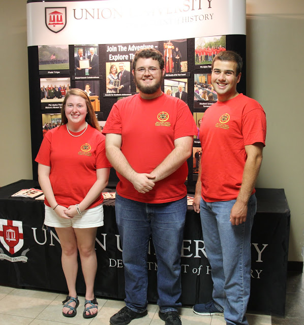 History student representatives at the Student Organizations Fair on August 17, 2015, stand together at the history department booth. They are (left to right) Kathryn Mitchell, Nicholas Hancock, and Allen Bradley.