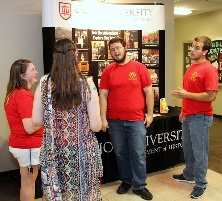 History student representatives at the history department's display booth talk to an interested classmate at the Student Organizations Fair on August 17, 2015. The history students are (left to right, wearing red Phi Alpha Theta T-shirts) Kathryn Mitchell, Nicholas Hancock, and Allen Bradley.