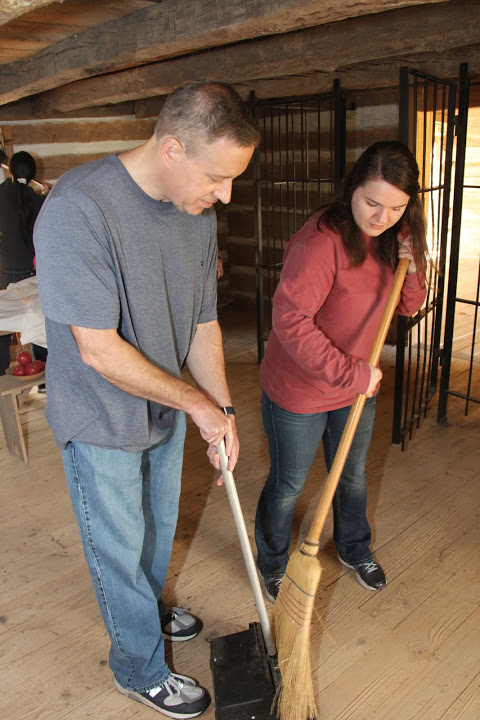 Jordan Sellers sweeps dirt into a long-handled dustpan that Dr. Henry Allen holds during the cleaning of a cabin room at Britton Lane Battlefield on November 3, 2015.