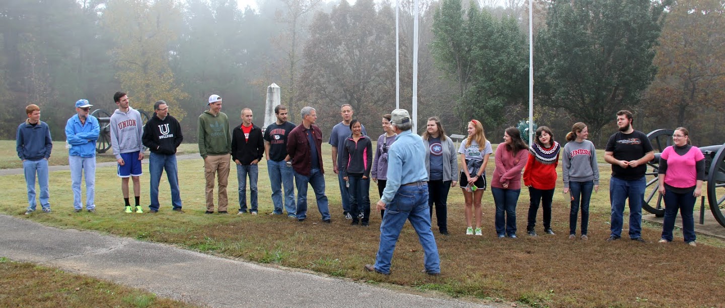 Britton Lane Battlefield Association President Jim Weaver (back to camera) divides members of the history department's Day of Remembrance group into four teams in preparation for firing a cannon on November 3, 2015. Group members are: (left to right) Gideon Ragland, Dr. Terry Lindley, Logan Smith, Dr. Keith Bates, Stephen Lewoczko, Devin Dean, Allen Bradley, Dr. David Thomas, Dr. Henry Allen, Katherine Cheshire, Emily Littleton, Jessica Barton, Ali Renckens, Jordan Sellers, Priscilla Porter, Beth Adams, Nicholas Hancock, and Hannah Conway.