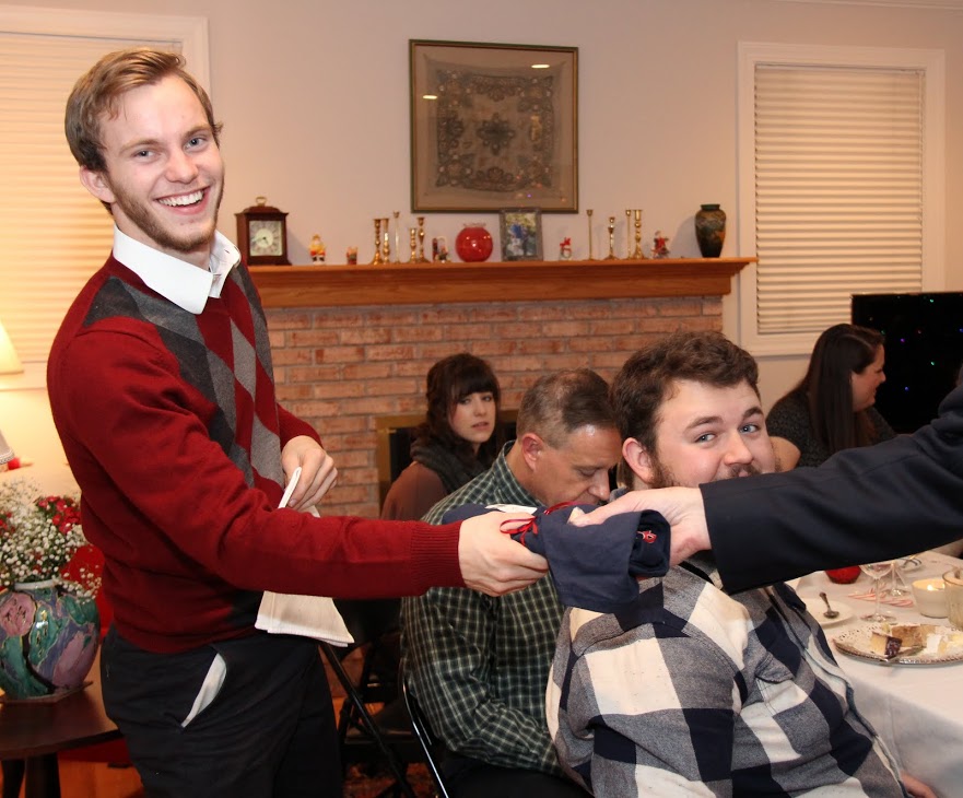 History major Seth Reid accepts his Phi Alpha Theta T-shirt from Dr. Stephen Carls at the history department's Christmas dinner on December 10, 2016. Nicholas Hancock (wearing black, gray, and white plaid shirt) looks on.