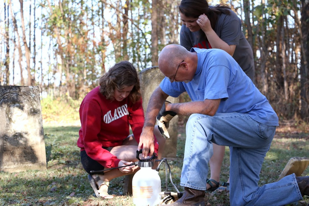 Dr. Kelvin Moore (right) and Beth Adams prepare a pump sprayer to clean tombstones at Salem Cemetery on November 1, 2016. Emily Littleton looks on with interest. Photo by Elizabeth Wilson