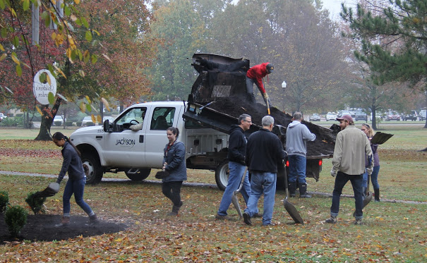 Union University participants in the history department's community service project at Liberty Garden Park place mulch around shrubs on November 7, 2017. They are (left to right) Katherine Cheshire, Lydia Black, Dr. Keith Bates, Dr. David Thomas (back to camera) Dr. Henry Allen (back to camera), Luke Sower, and Ali Renckens. Seth Reid, standing on the the truck's dump body, pushes mulch toward the workers.