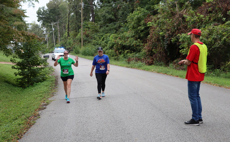 Robert Briley (right) cheers on two participants in the Racing So They Can Ride event on Saturday, September 18, 2021, while a City of Jackson police vehicle provides safety protection behind them.