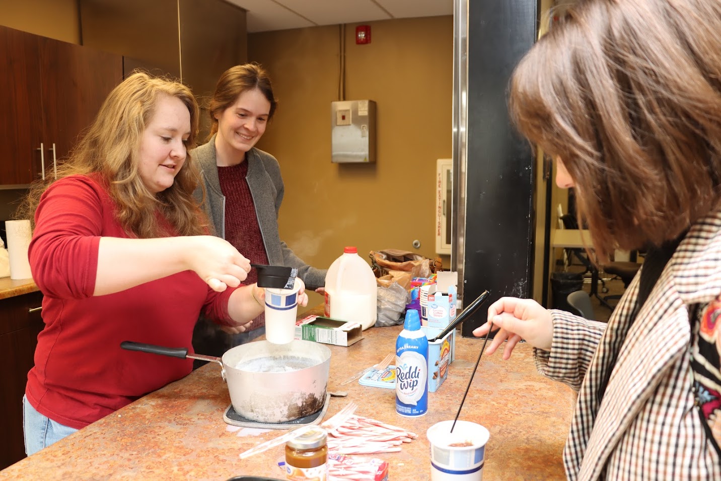 Rutledge Honorary History Club President Breanna Edmiston (left) serves hot chocolate to Sophia Keskeys (right) at the club's fall plenary meeting on November 14, 2022. Samantha Poore (center) helps in the kitchen.