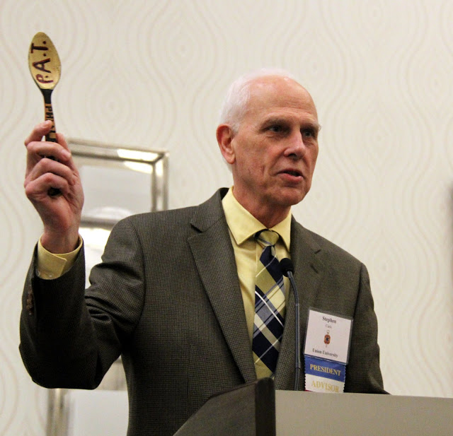 Dr. Stephen Carls prepares to pass the Phi Alpha Theta presidential spoon of authority to Dr. Jochen Burgtorf at the society's Presidential Banquet on January 9, 2016.