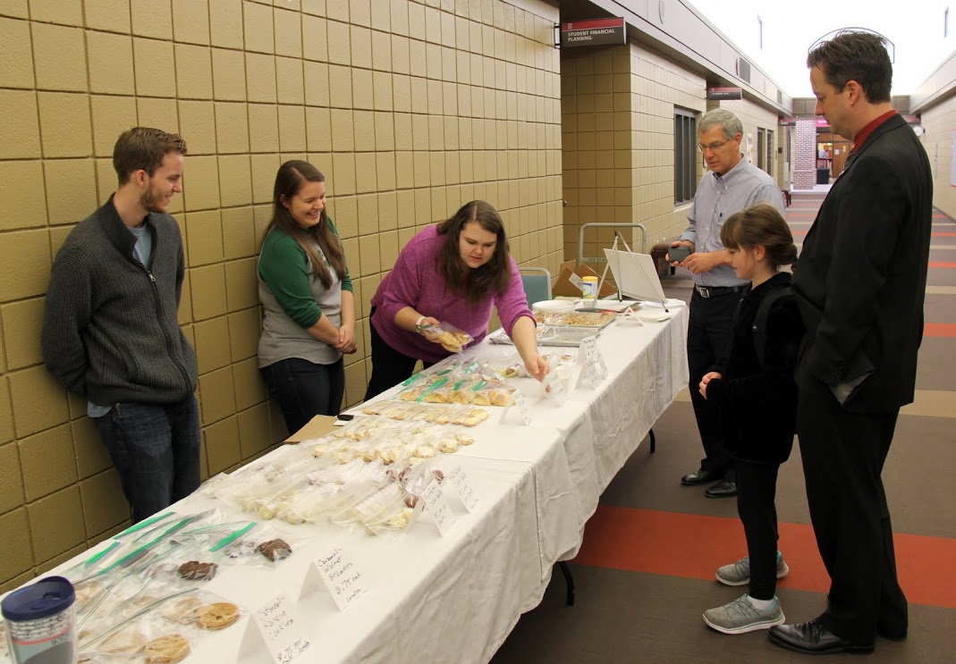 Phi Alpha Theta member Jessica Barton gathers some sale items for Dr. David Thomas (wearing light blue shirt) at the Phi Alpha Theta-sponsored Franco-American Confection and Bake Sale on March 22, 2017. Salespersons Seth Reid (left) and Jordan Sellers (second from left) observe. Dr. Jason Garrett, Dean of the Union University School of Business, stands with his daughter on the right.