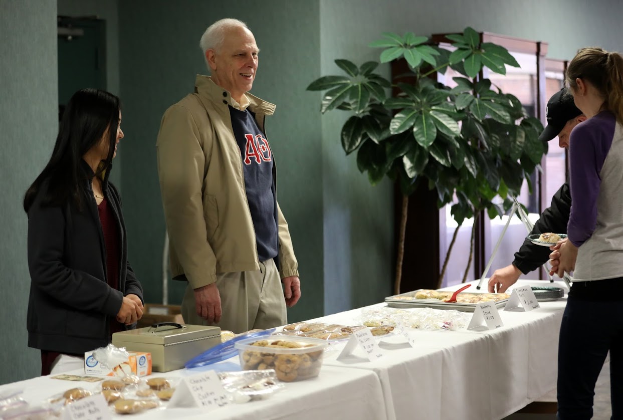Katherine Cheshire (left) and Dr. Stephen Carls (also behind the table) talk to customers in the chapel foyer during the Phi Alpha Theta bake sale on April 11, 2018. Photo by Kristi Woody
