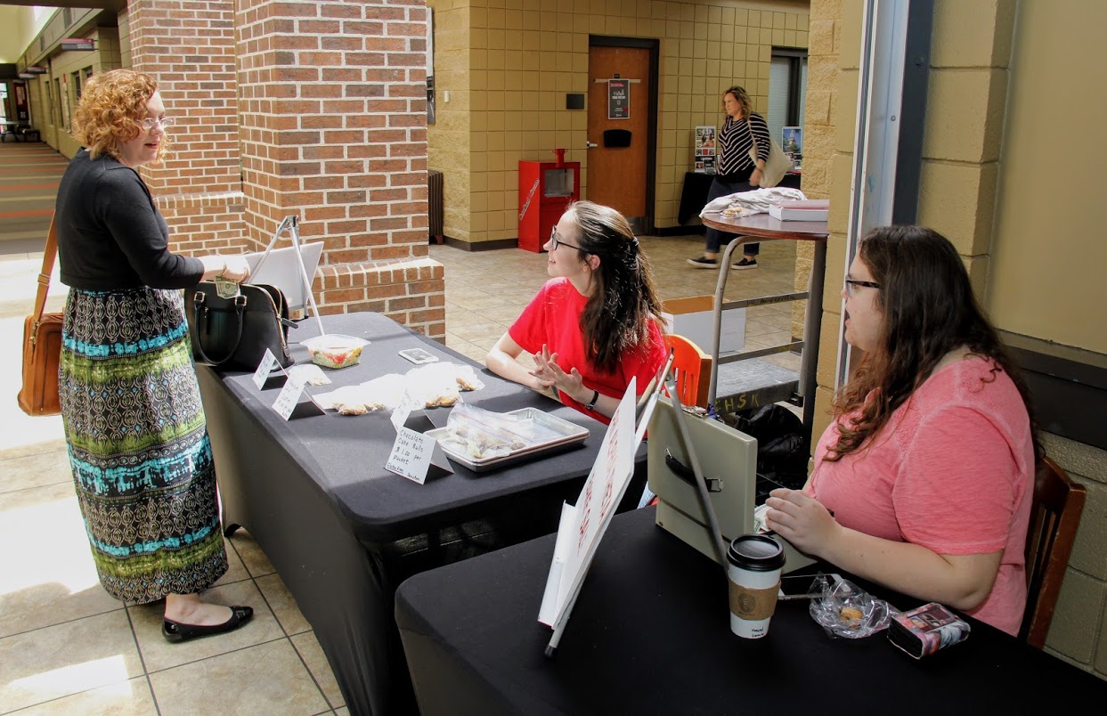 Lauren Butler (seated, left) and Jessica Barton (seated, right) converse with a customer at the Phi Alpha Theta bake sale near the Lexington Inn on April 11, 2018.