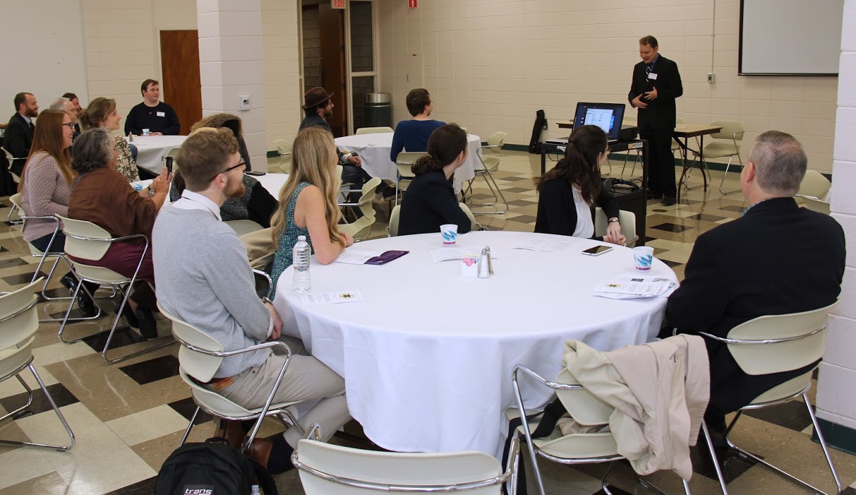 Dr. John Henris, the Phi Alpha Theta conference coordinator, welcomes attendees to the campus of the University of Arkansas at Monticello on April 7, 2018. Seated at the table in the foreground are Union University participants, including (left to right) Luke Sower, Ali Renckens, Leah Atkins, Lauren Butler, and Dr. Henry Allen.