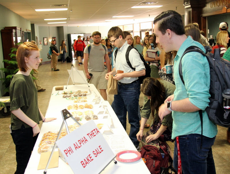 Savannah Wright (left) prepares to make a sale in the chapel foyer to Phi Alpha Theta member Mac Hazlerig (front right) at the Phi Alpha Theta bake sale on April 10, 2019.