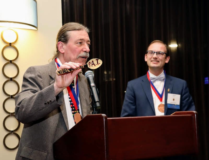 Phi Alpha Theta President Dr. Clayton Drees (left) prepares to pass the spoon of authority to incoming president Dr. Jacob Blosser (right) at the society's Presidential Banquet on January 4, 2020.