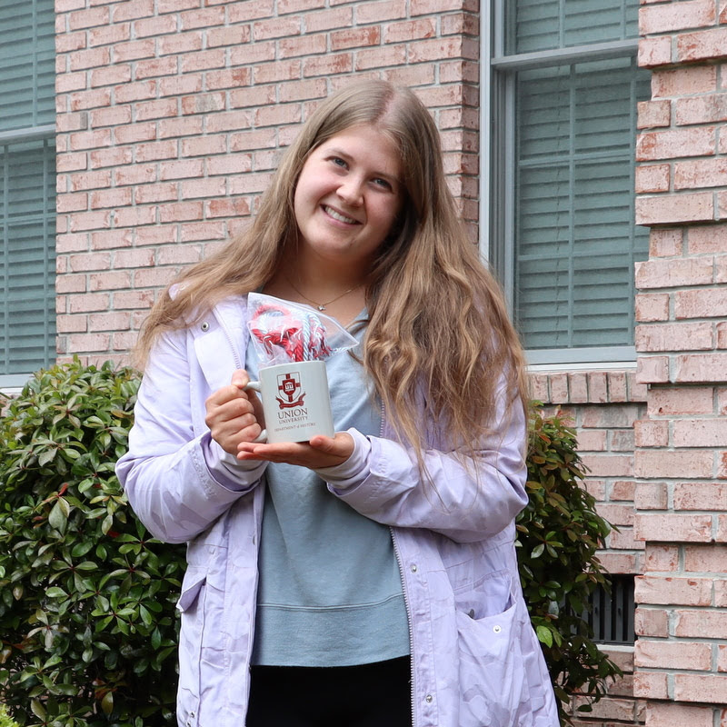Graduating history major Hannah Ratliff holds her Phi Alpha Theta honor cord and history department mug in May 2020.