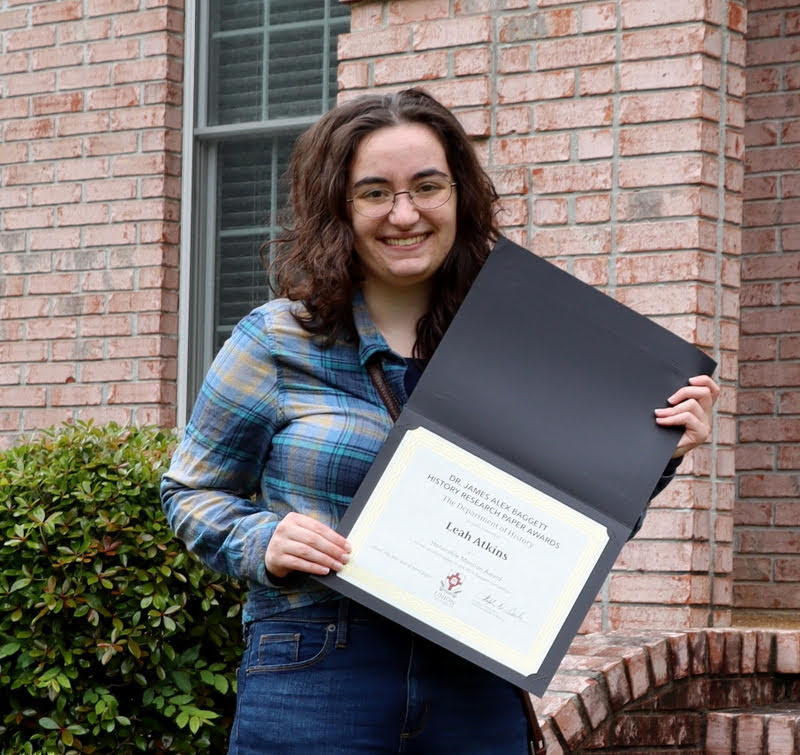 Leah Atkins displays her Dr. James Alex Baggett History Research Paper Competition award certificate during a brief presentation ceremony at Dr. Stephen Carls's home in May 2020.