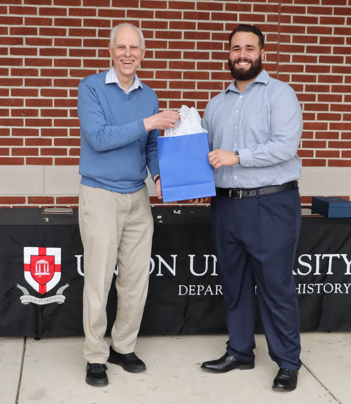 Dr. Stephen Carls (left) presents a graduation gift award to graduating history major Nicholas Terra at the History Department Awards Program on April 28, 2022.