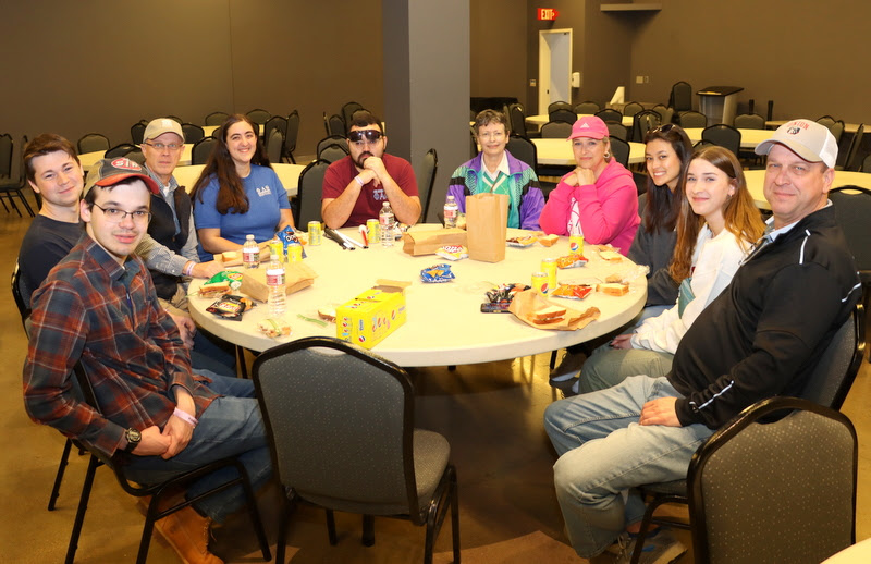 The participants in the Phi Alpha Theta-sponsored visit to Discovery Park of America on April 1, 2023, have lunch together in a reserved dining room. They are (starting on the front left and going clockwise) William Houston, Noah Kea, Robert Briley, Joy Brown, Chris Young, Dr. Alice-Catherine Carls, Carol Lynn Jahnke, Makayla Baker, Madeline Jahnke, and Steve Jahnke. Dr. Stephen Carls took the photo.