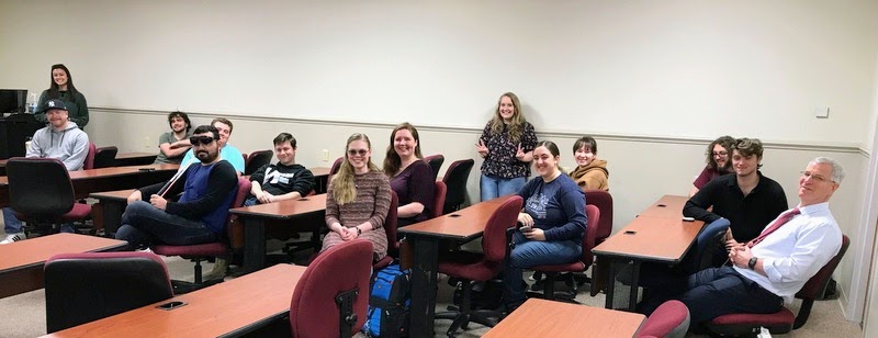 Attendees at the Phi Alpha Theta-sponsored surprise retirement party for Dr. Stephen Carls wait for his arrival on April 24, 2023. They are (left to right) Makayla Baker, John Garland, Jonathan Sanders, Chris Young, Austin Alexander (directly behind Young in turquoise shirt), Noah Kea, Anna Guelcher, Abigail Gilbert, Breanna Edmiston (standing), Joy Brown, Sophia Keskeys, Nicholas Palmer, Jacob Frederick, and Dr. David Thomas.