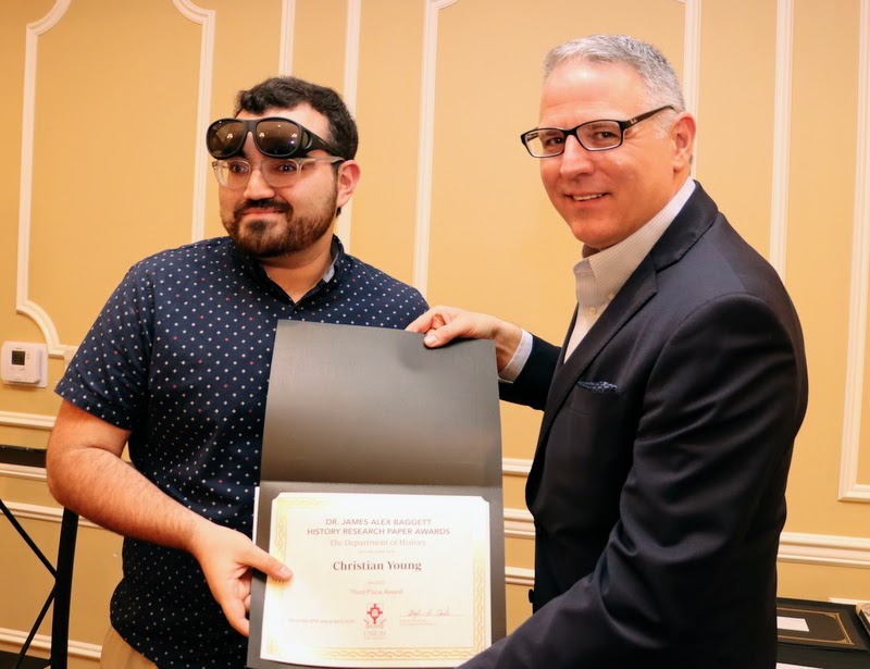 Christian Young (left) receives the third place prize (a certificate and a check) in the Dr. James Alex Baggett History Research Paper Competition from Dr. Keith Bates at the History Department Awards Banquet on April 27, 2023.