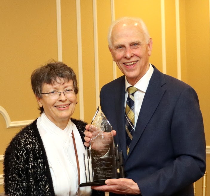 Dr. Stephen Carls stands with his wife Dr. Alice-Catherine Carls as she presents him with a crystal award for his retirement during her history awards banquet address on April 27, 2023.