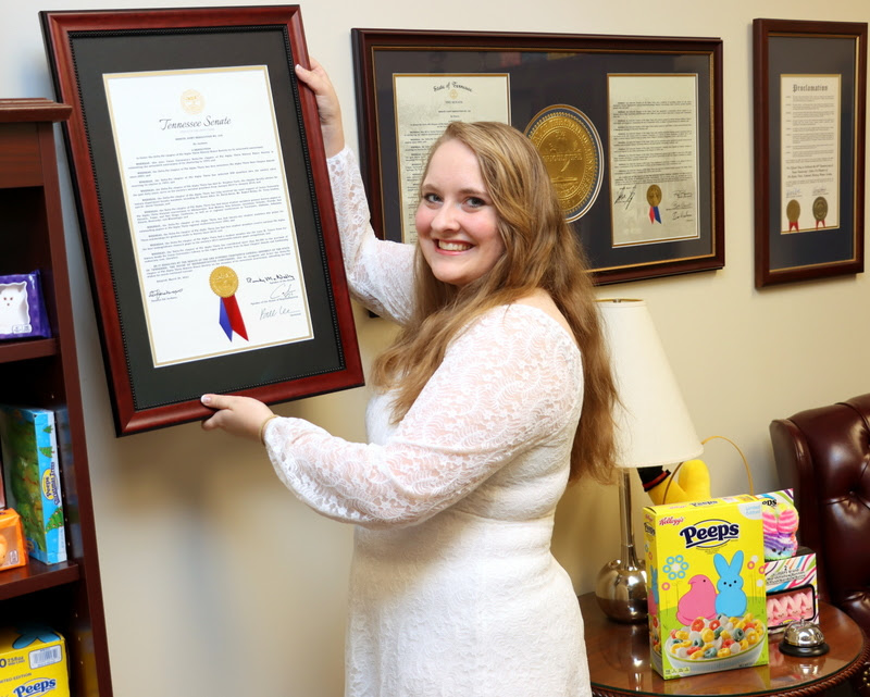 Delta-Psi Vice President Breanna Edmiston places on a Phi Alpha Theta wall in Dr. Stephen Carls's office on May 6, 2023, a Tennessee Senate Joint Resolution congratulating Union's Delta-Psi chapter on its 70th anniversary in 2023 (1953-2023). Since the Delta-Psi chapter is known as the Peeps chapter, many Peeps items also adorn Dr. Carls's office.