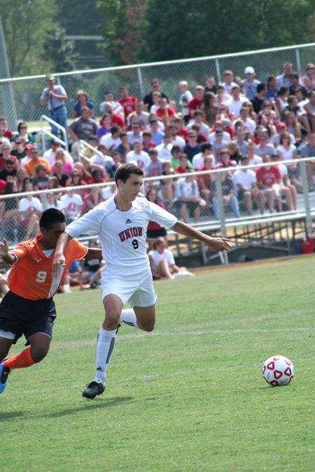 Guilherme Reis, freshman, dribbles the ball away from his Brewton Parker opponent. Watching him is a full crowd of fans enjoying Union's new soccer field stands. - Photo by Kristi McMurry Woody