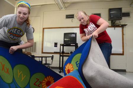 Elissa Weber, senior teaching English as a second language major, and Emily Maggard, English and elementary education double major, deliver large reading rugs to Holt Elementary teachers' class rooms who have been relocated to Lloyd Wood Middle due to tornado damage. - Photo by Beth Spain