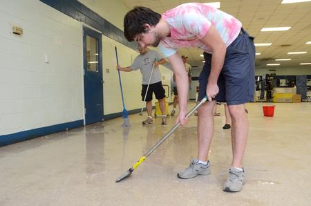 Stephen Capps, senior Biblical languages major, scrapes wax from the cafeteria floor at Lloyd Wood Middle School. Holt Elementary School will soon begin school here after water damage forced them to move to this previously vacant school building. - Photo by Beth Spain