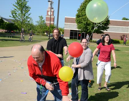 Art department faculty members Lee Benson, Steve Halla, Melinda Posey and Haelim Allen laugh together as they help take down an arch of more than 1,600 balloons that floated over campus. - Photo by Jacob Moore