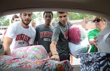 Soccer players Guilherme Reis, Stevie Reddick and Juan Rios help unpack a car with Kelsie Meadows, senior philosophy major, during new student move-in day. - Photo by Jacob Moore