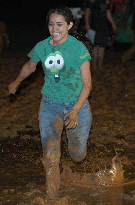Junior Estella Argueta runs a relay race through the mud during the Young Alum's Midnight Mudness. - Photo by Jonathan Blair