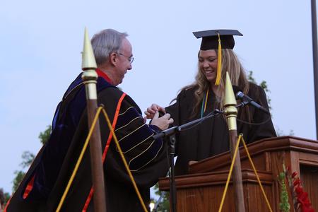 Anika Strand, 2013 senior class president and social work graduate,  presents David S. Dockery, president of the university, with a dog tag that represents the golden dog statue given by the senior class. - Photo by Matt McDaniel