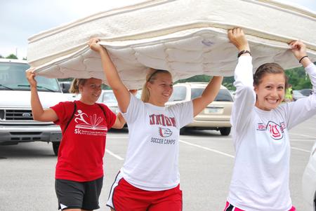 Paula Arias (right), sophomore math major, Emily Wagner (middle), sophomore athletic training major, and Dionna Linn, senior athletic training major, help move a freshman's mattress into his dorm on new student move-in day.  - Photo by Anne Richoux