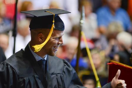 Krister Andreassen, sport management (marketing) graduate, gives a thumbs up to cheering friends as he crosses the stage to receive his diploma at Spring Commencement Services. - Photo by Meg Rushing