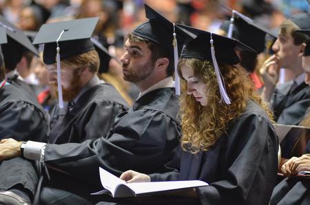Sarah Halbrook,right, English graduate looks through the program listing the 630 graduates walking in the 189th annual Spring Commencement Services, held at the Oman Arena due to rain.  - Photo by Emily Stookey