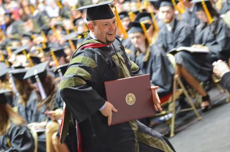 Collin Cantrell, doctor of pharmacy graduate, shows off his degree to onlooking friends and family at Spring Commencement Services. - Photo by Emily Stookey