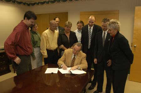 The core migration team watched President Dockery sign an agreement with Datatel for a new campus information system.  Pictured behind President Dockery from left to right: Cam Tracy, Connie Magers, Mike Smith, Gary Carter, Karen McWherter, David Porter, Datatel sales rep Matt Alonzo, John David Barham, and Katrina Bradfield. - Photo by Jim Veneman