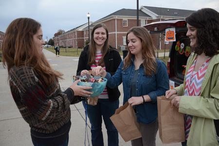 Abi Rhodes, sophomore education major, hands out candy to Rachel Witt, sophomore nursing major, Abby Wills, sophomore applied linguistics major, and Emily Savage, sophomore TESL and music major, during Trunk or Treat hosted by the Student Government Association's sophomore council. - Photo by MiKalla Cotton