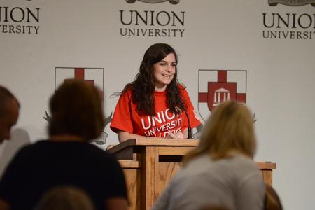 Mallory Lamm, sophomore social work major, welcomes new students to orientation and opens the morning with prayer in the Carl Grant Events Center. - Photo by Meg Rushing