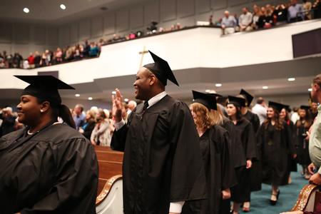 Dominique Willingham, broadcast journalism graduate, waves to friends during the processional into fall commencement services.  - Photo by Kristi McMurry Woody