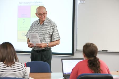 Ken Newman, adjunct professor of educational leadership, hands out papers at the start of class. - Photo by Kristi McMurry Woody