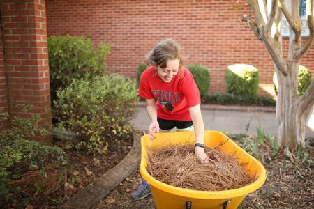 Kate Pryor, senior special education major, works in the flower beds at Augustine School during Campus and Community Day. - Photo by Kristi McMurry Woody