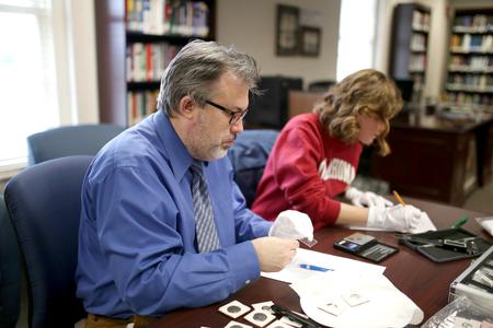 Gavin Richardson, professor of English, helps Beth Adams, senior English major, with her research project of cleaning and cataloguing a rare coin collection. - Photo by Kristi McMurry Woody