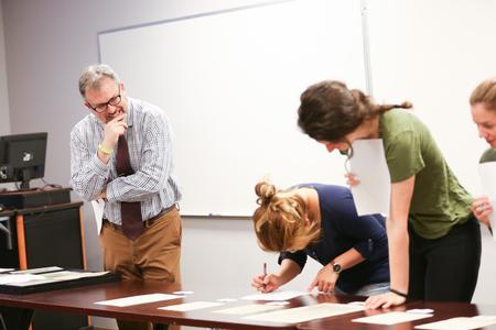 Gavin Richardson, professor of English, watches as his students examine authentic 16th century Bible leaves for an exercise in his class. - Photo by Kristi McMurry Woody