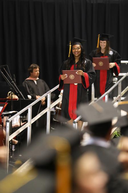 Kelsey Robinson, teaching and learning and interdisciplinary studies graduate, smiles with her diploma as she walks back to her seat during spring commencement services.  - Photo by Kristi McMurry Woody